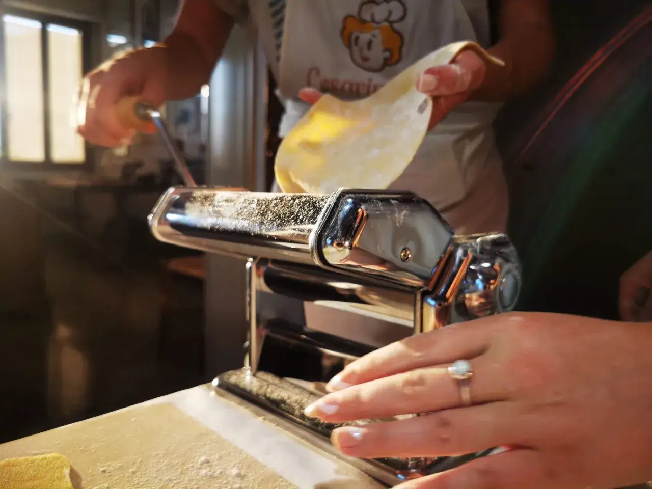 Mani che preparano pasta fresca con una macchina per la pasta, un'esperienza tipica dei corsi di cucina a Venezia.
