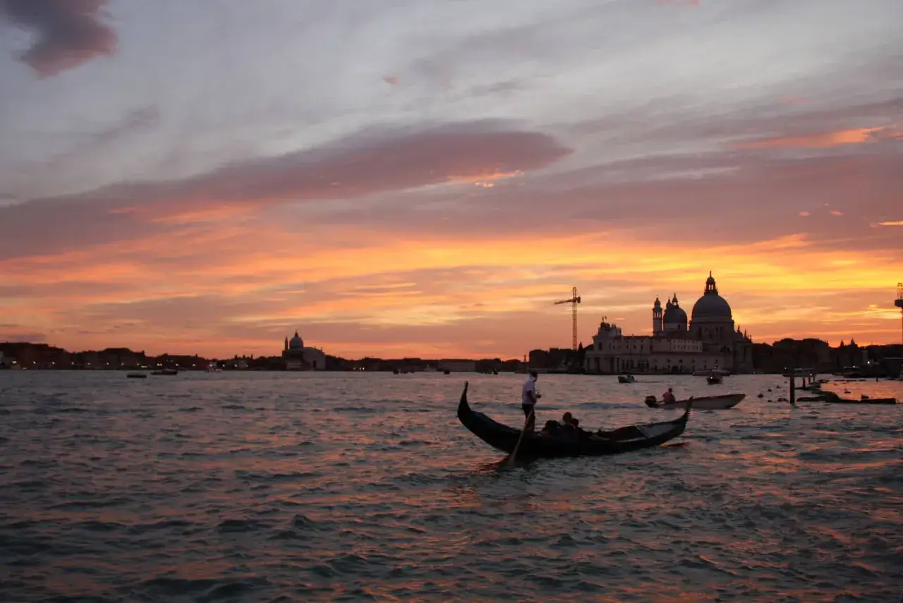 Tramonto infuocato su Venezia, città dell'amore, con gondole che scivolano sull'acqua e cupole maestose all'orizzonte.