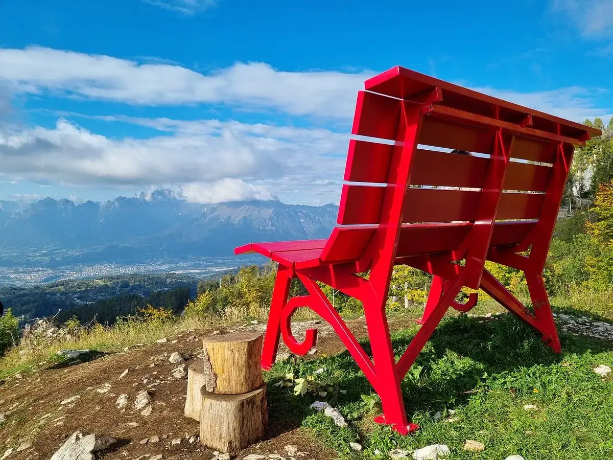 La panchina gigante sul Nevegal, rossa e imponente, domina un panorama mozzafiato di montagne e vallate sotto un cielo azzurro.