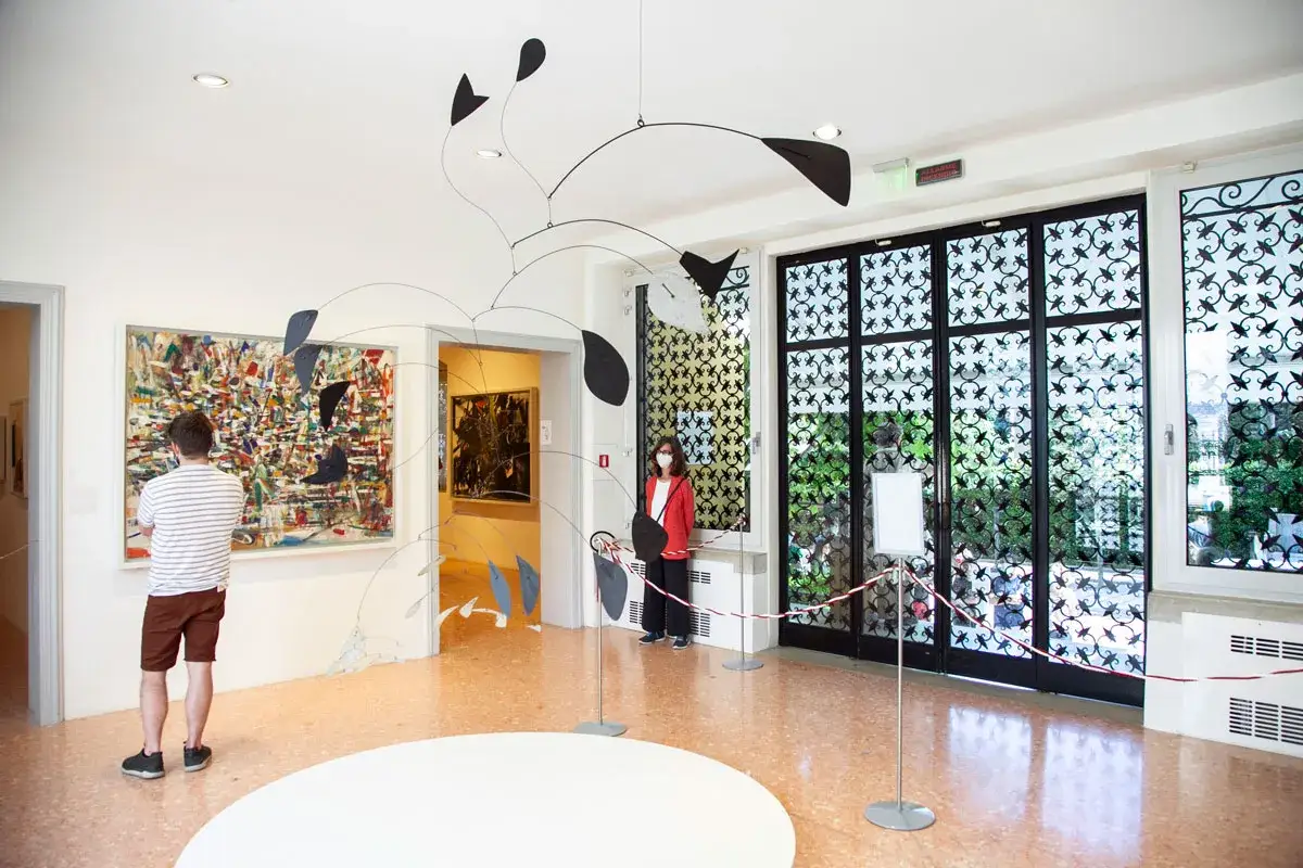 Un uomo ammira un quadro astratto, mentre una donna osserva una scultura mobile. Un'atmosfera d'arte al Peggy Guggenheim di Venezia.