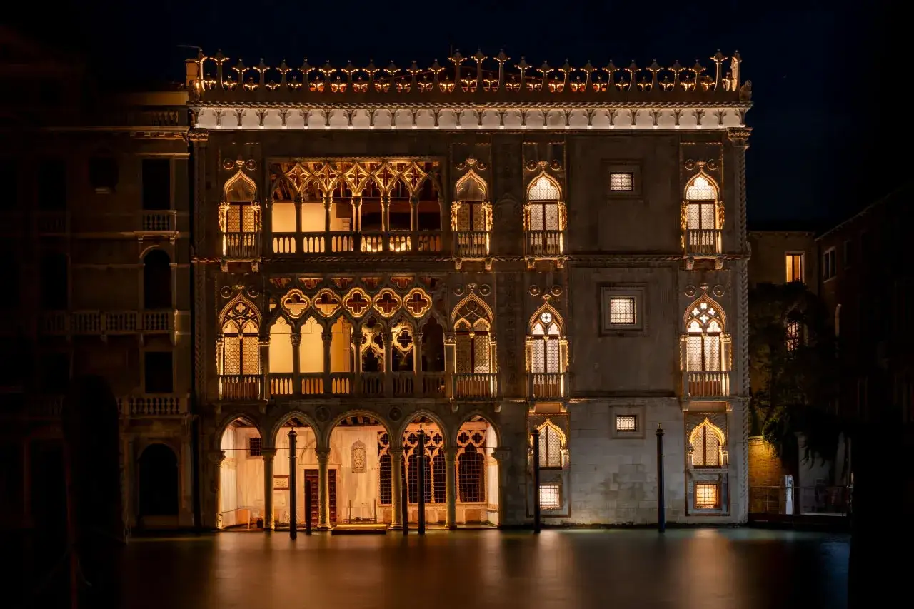 Palazzo Ca' d'Oro, un gioiello illuminato di notte a Venezia, con le sue finestre dorate che riflettono sull'acqua.