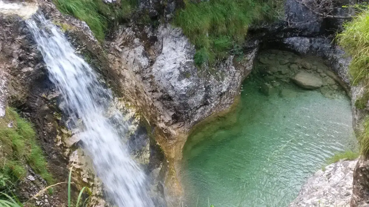 Cascata che si getta nel lago del Mis, con acque cristalline e rocce ricoperte di vegetazione.