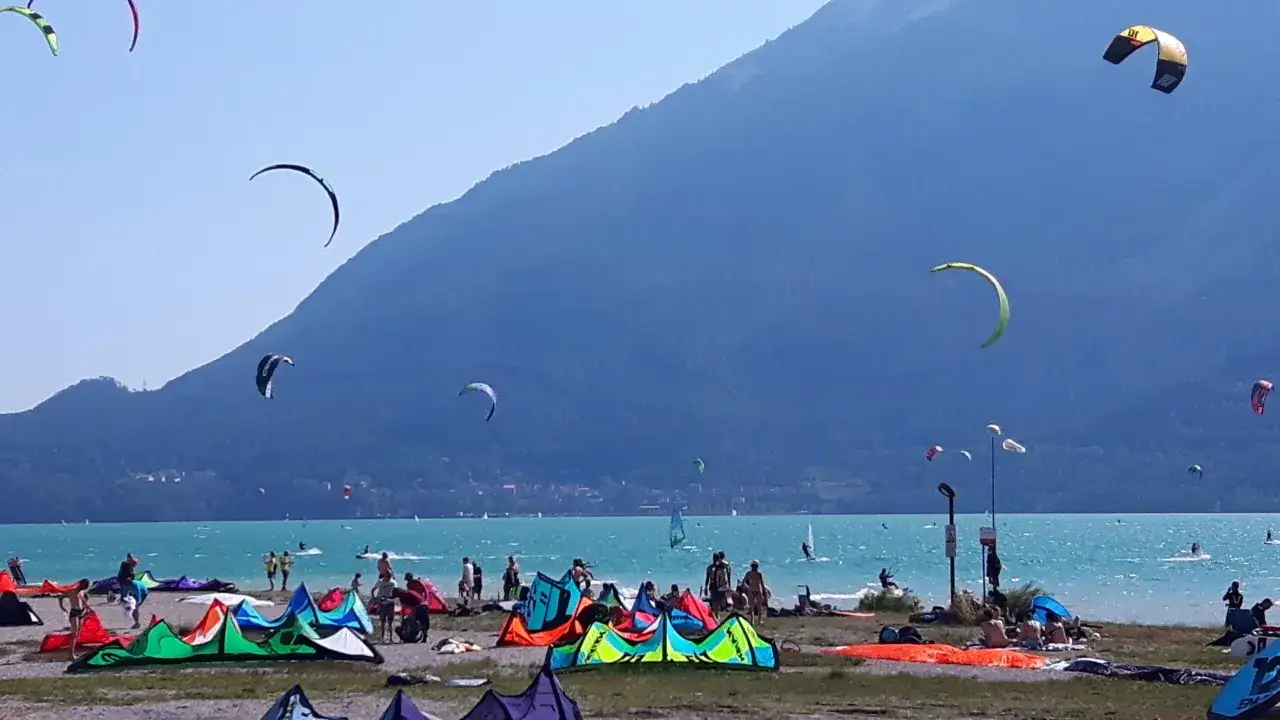 Colorate vele da kitesurf riempiono il cielo azzurro sopra la spiaggia del lago di Santa Croce, con persone che si godono la giornata.