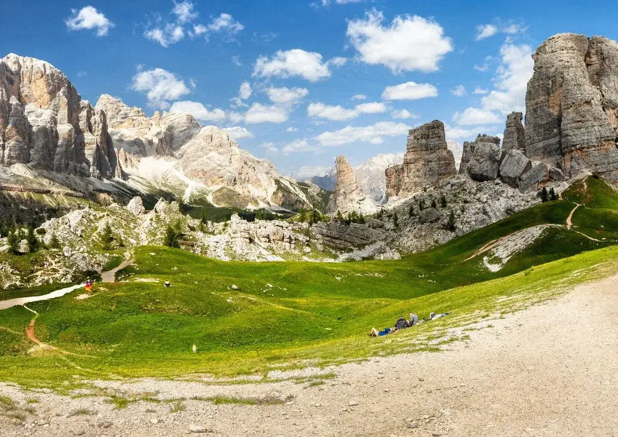 Un paesaggio mozzafiato delle Cinque Torri Dolomiti, con vette imponenti, prati verdi e un cielo azzurro punteggiato di nuvole.