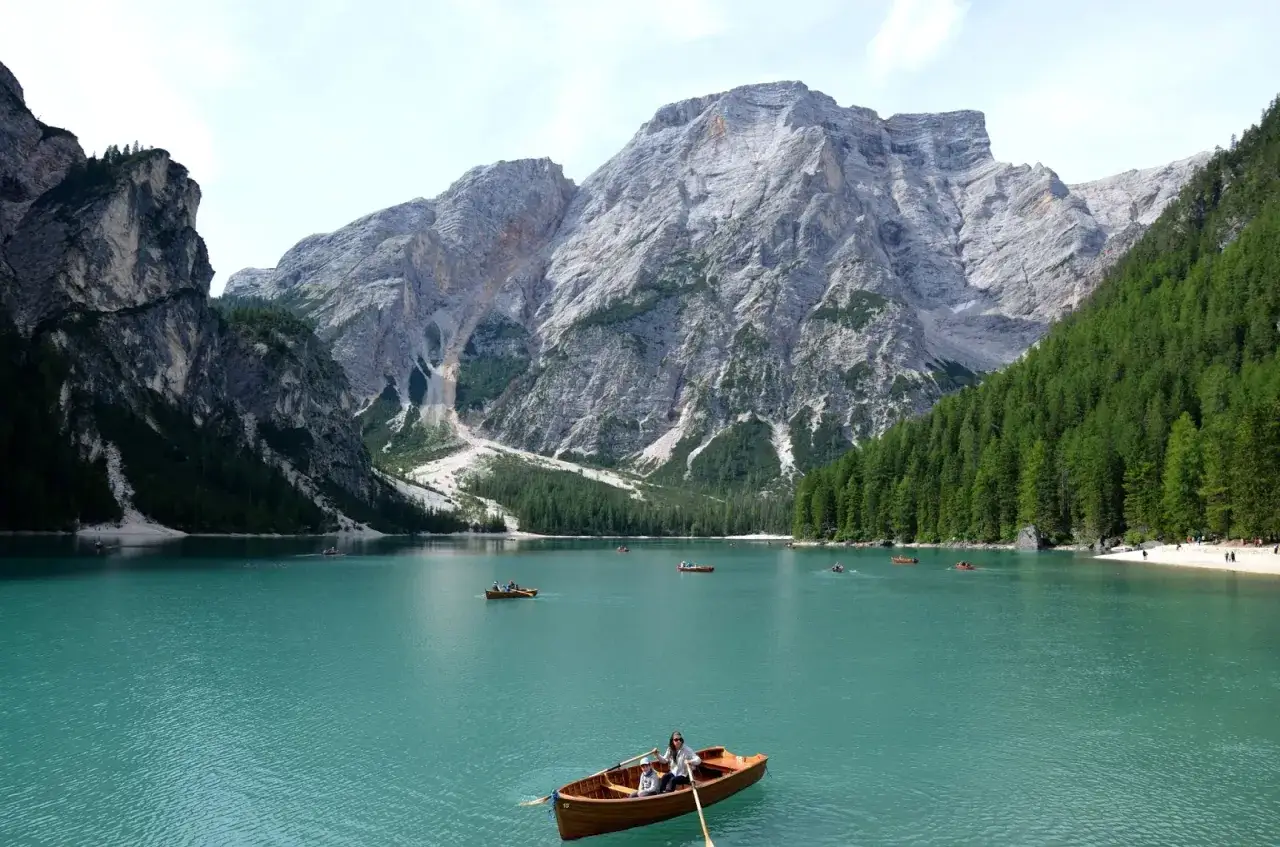 Barche sul lago turchese ai piedi delle maestose montagne veneto, con boschi di conifere e vette rocciose.