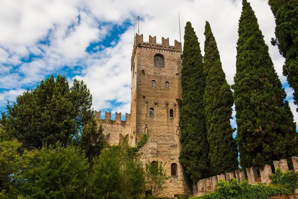 Torre medievale circondata da cipressi e vegetazione, con merlature e finestre ad arco. Un scorcio di cison di valmarino.