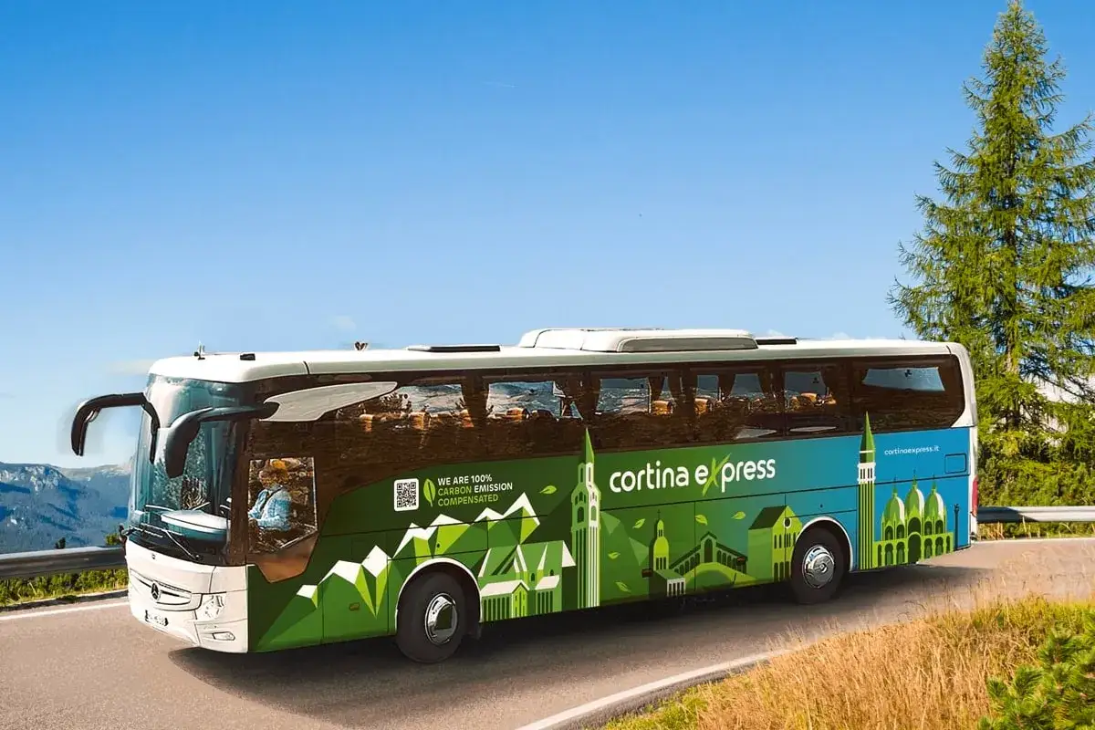Un bus Cortina Express, con grafica che unisce Venezia e le montagne, viaggia su una strada panoramica.