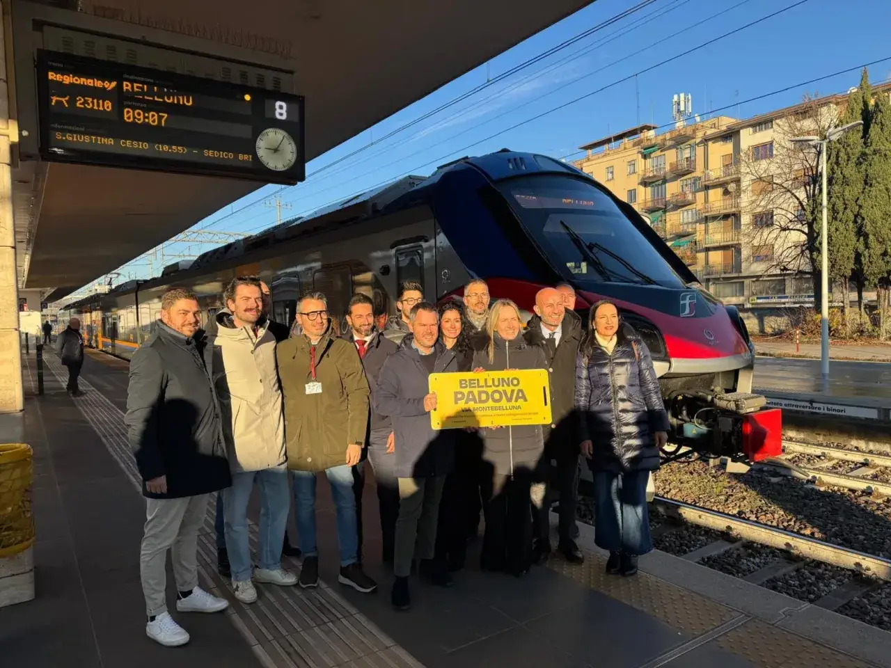 Gruppo di persone festeggia l'avvio del collegamento ferroviario Belluno-Padova, un nuovo viaggio da Padova a Treviso e oltre.