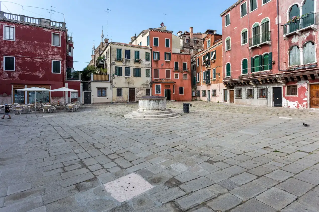 Una piazza veneziana con un pozzo al centro, circondata da case colorate. A Venezia, queste piazze si chiamano campi.
