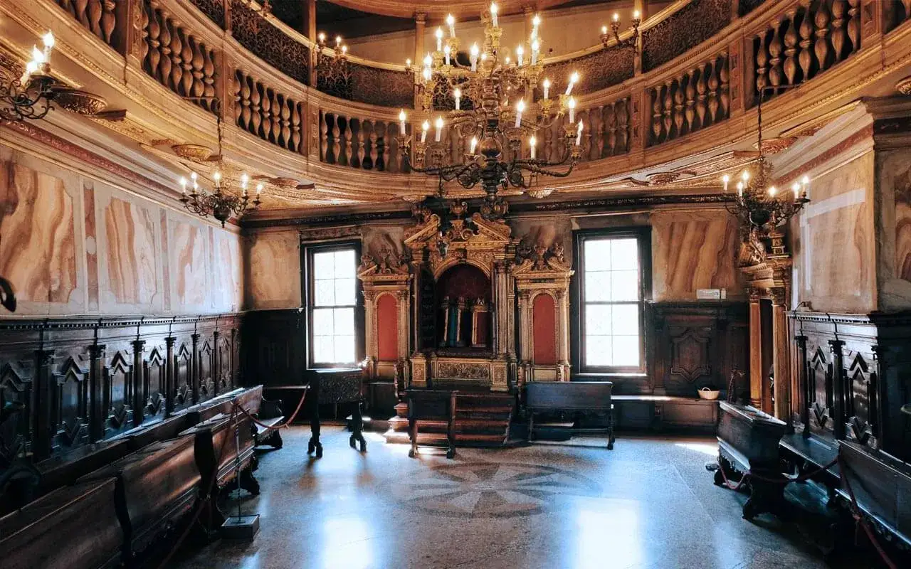 Interno di una sinagoga nel ghetto ebraico di Venezia, con arredi in legno scuro, un maestoso lampadario e l'Arca Santa dorata.
