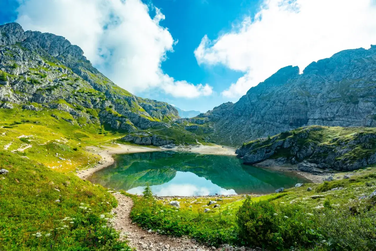 Sentiero panoramico verso un lago alpino turchese, incastonato tra imponenti vette rocciose. Un vero gioiello dell'alta via Dolomiti pi&ugrave; bella.