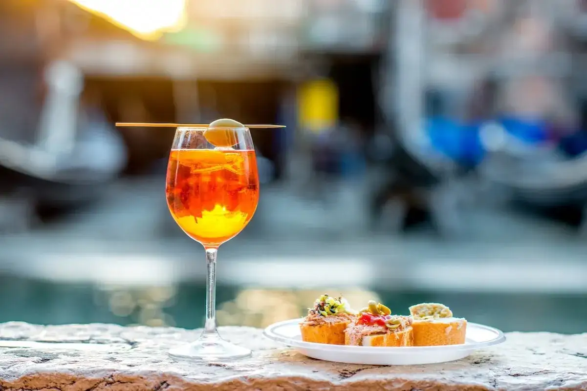 Un bicchiere di Spritz con olive e fettine d'arancia, accompagnato da tartine, perfetto per un aperitivo con le giuste dosi per spritz.
