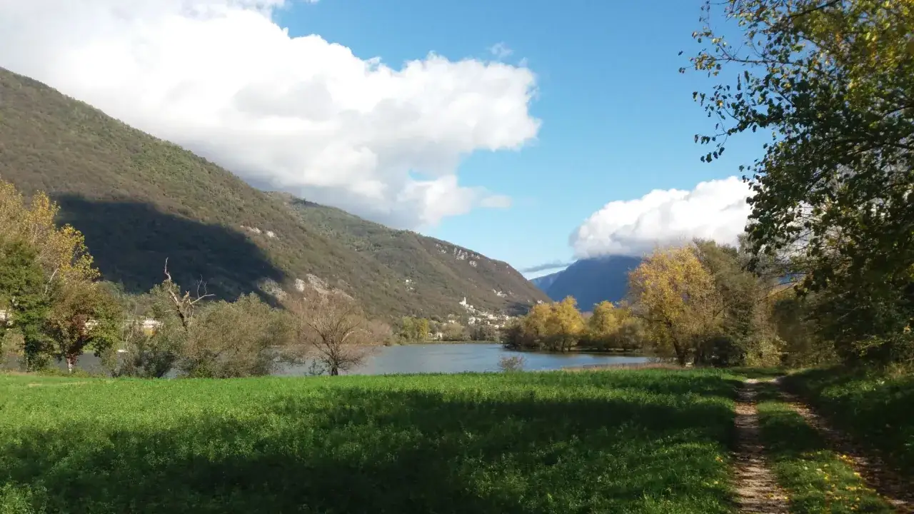 Sentiero sterrato per passeggiate in montagna in Veneto, con lago e colline verdi sotto un cielo azzurro con nuvole bianche.