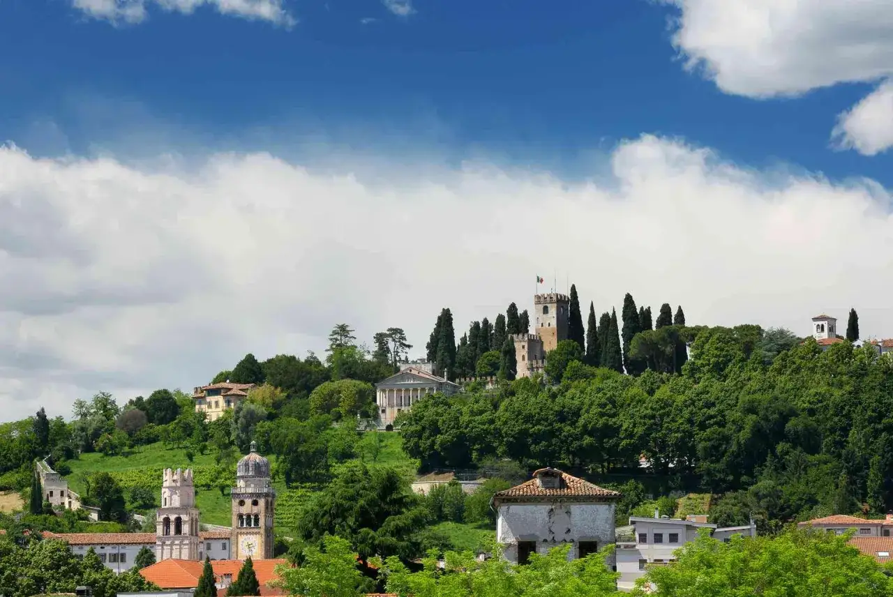 Panoramica di Conegliano cosa vedere: castelli, torri e ville storiche immerse nel verde, sotto un cielo azzurro con nuvole bianche.