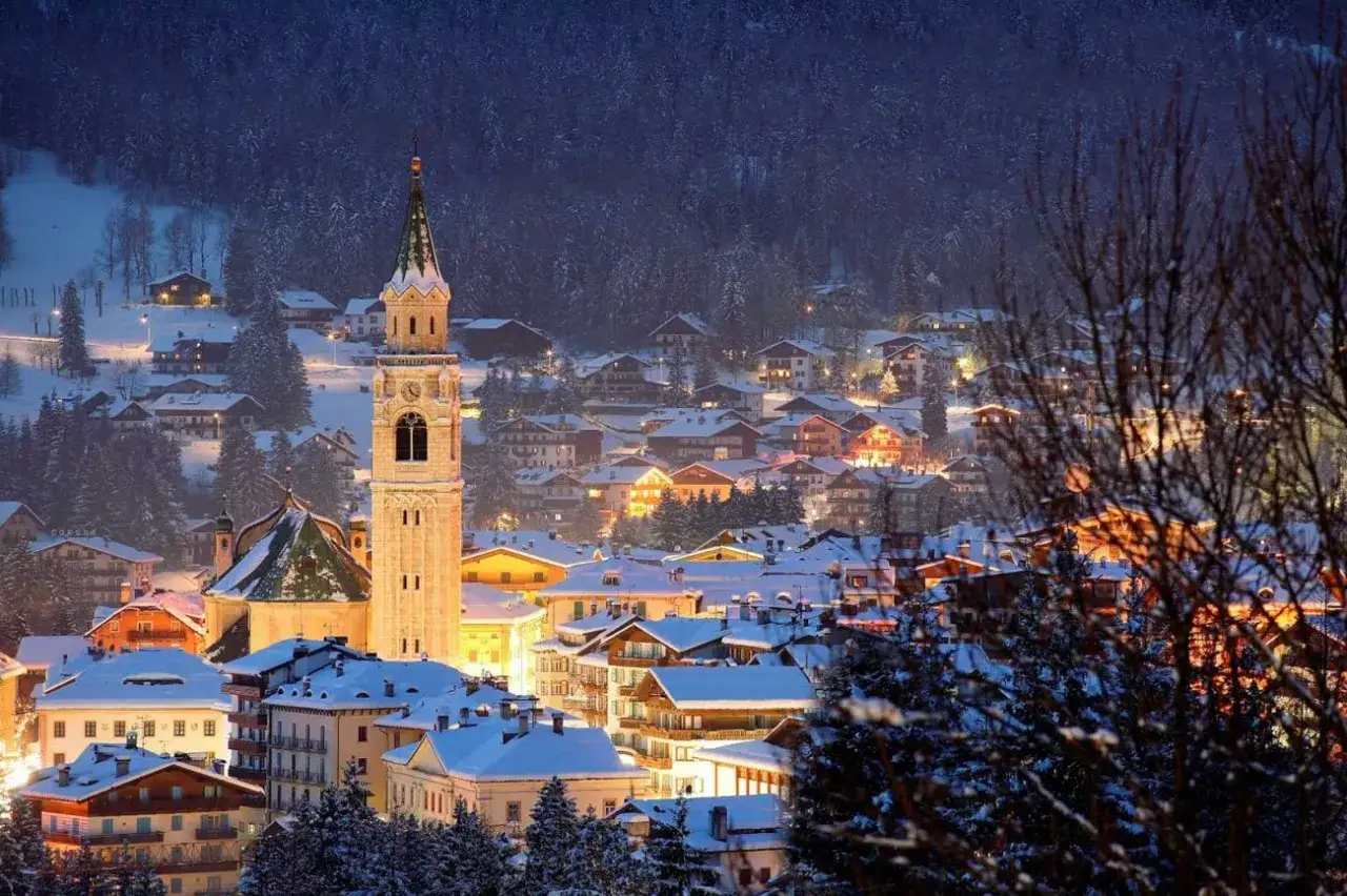 Cortina d'Ampezzo a Natale: un borgo innevato illuminato, con un campanile che svetta tra le case e i boschi. Magia alpina.