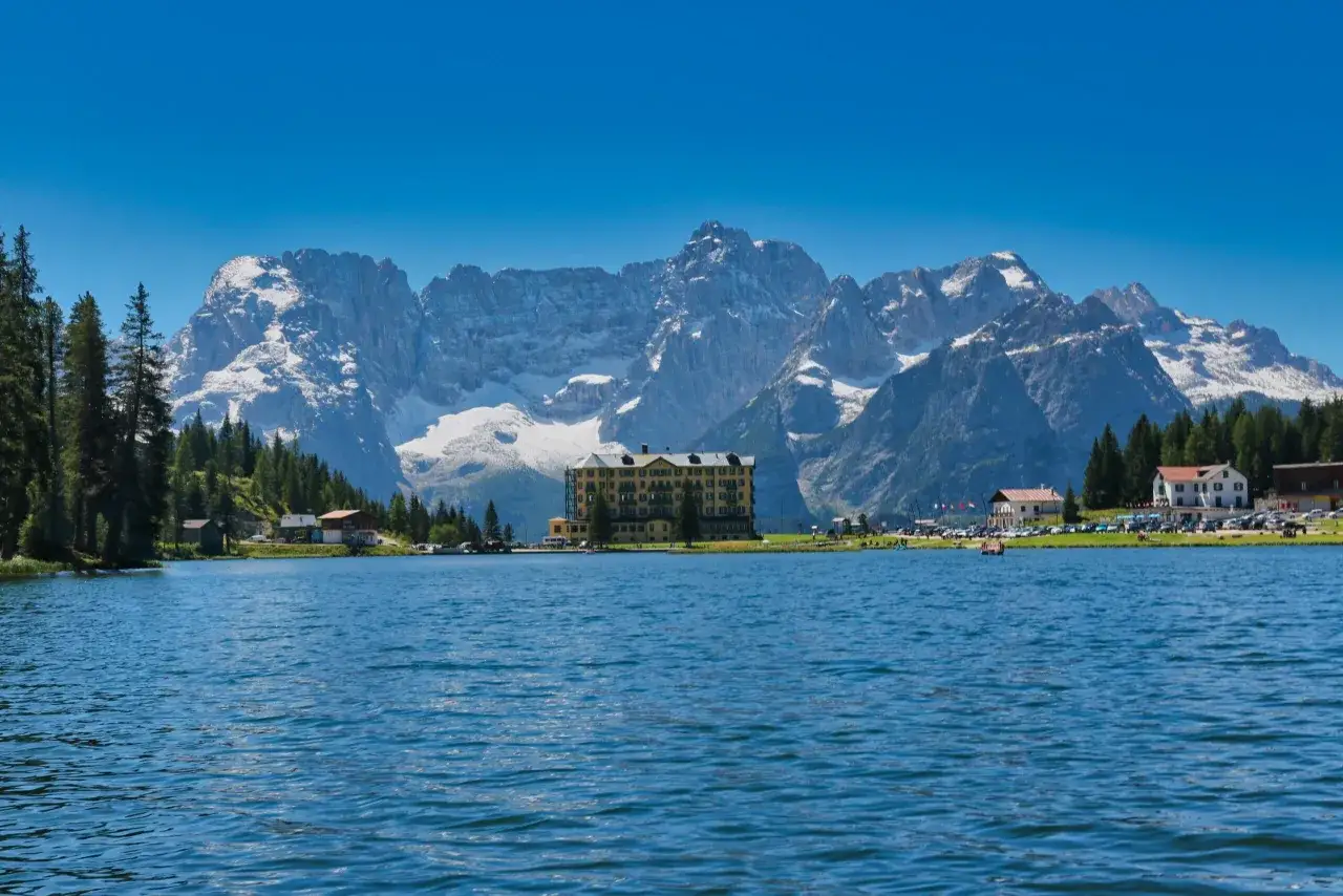 Il lago di Misurina, incastonato tra le maestose Dolomiti, con un grande hotel giallo e montagne innevate sullo sfondo.
