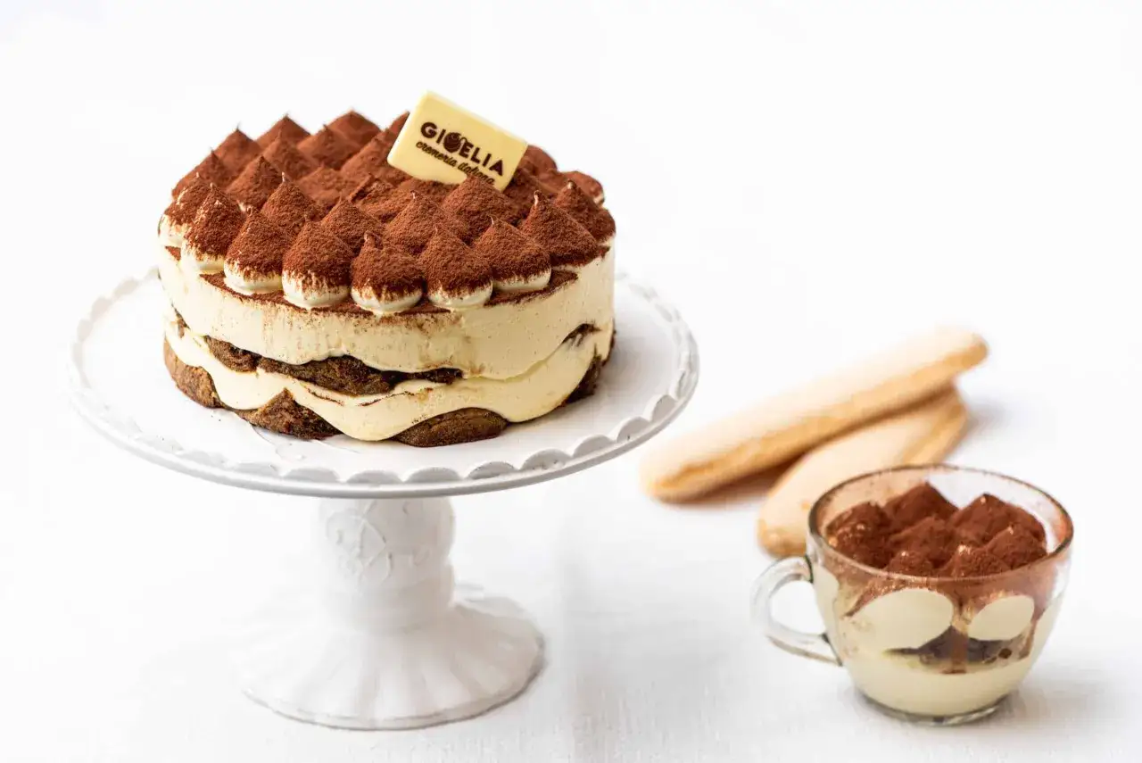 Torta tiramis&ugrave; su alzata, con savoiardi e una coppetta. Perfetta per scoprire come si fa il tiramis&ugrave;.