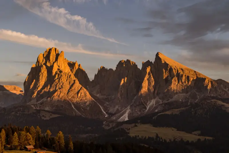 Le maestose **Dolomiti Rosse** illuminate dal sole al tramonto, con cime aguzze e pendii boscosi.